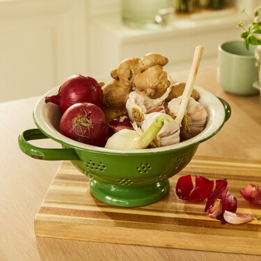 Grüne Schale auf einem Holzschneidebrett mit Zutaten für eine gesunde Ernährung, darunter rote Zwiebeln, Knoblauch und Ingwer.