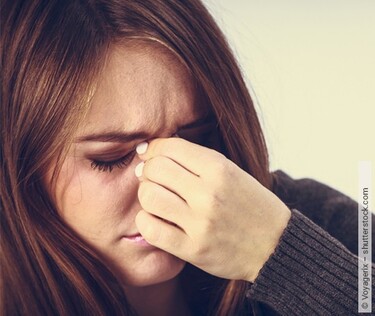 Wegen einer Pansinusitis fasst sich eine Frau an die Nasennebenhöhlen.