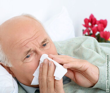 Senior mit Sinusitis putzt sich die laufende Nase.