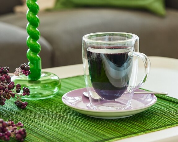 Natürliche Gesundheitsförderung mit Holunderbeersaft, ideal während der Erkältungszeit. Transparente Tasse mit Holunderbeersaft steht auf einem grünen Tischset zur natürlichen Unterstützung des Immunsystems.